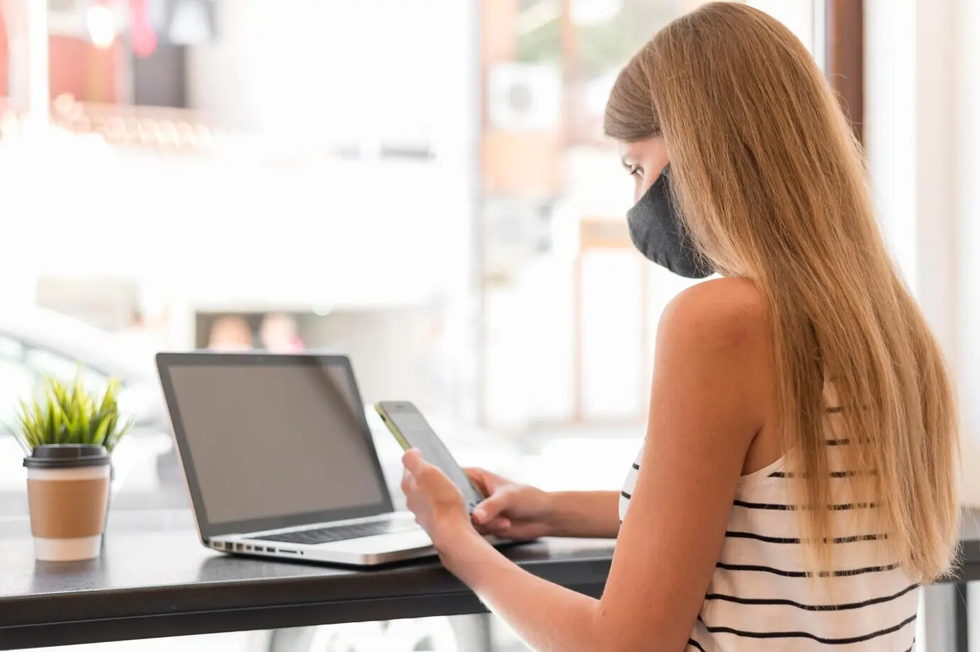 Портрет женщины в маске с ноутбуком на террасе.